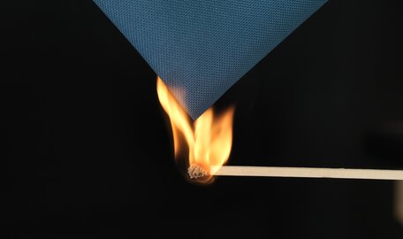 Flamme eines Feuerzeugs züngelt an dunkelblauem Textil