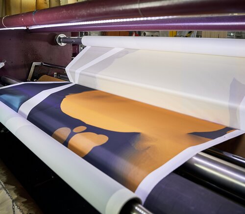 Mit einer Maschine wird weißer Zeltstoff im Sublimationsdruckverfahren bedruckt.