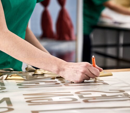 Per Hand wird das Motiv aus Vinyl-Folie ausgelöst, um es mit einer Heizpresse auf den Zeltstoff zu übertragen.