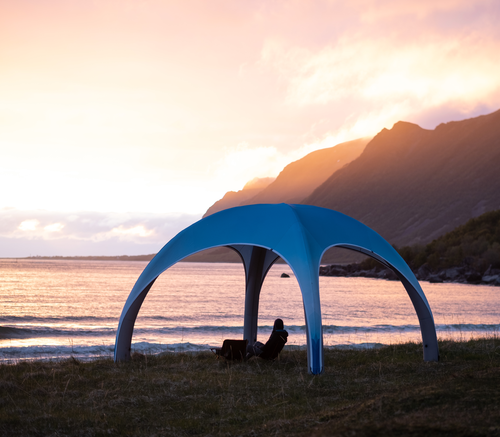 Eine Person sitzt bei Sonnenuntergang unter einem aufblasbaren Zelt am Meer.