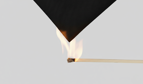 Ein Streichholz wird unter ein Stück schwarzes Zelttextil gehalten, hellgrauer Hintergrund