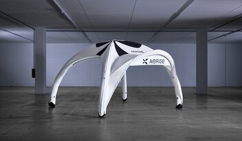 Weißes aufblasbares Zelt mit schwarzer Bedruckung und Vordach in leerer Produktionshalle