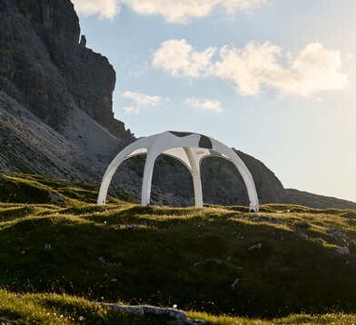 Aufblasbares Zelt in der Farbe weiß mit bedrucktem Dach auf felsiger Wiese, leichtes Gegenlicht