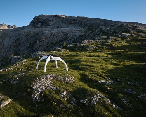 Ein weißes aufblasbares Zelt steht auf einer grünen Wiese in einer schroffen Berglandschaft.