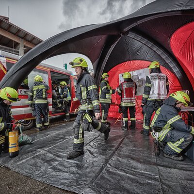 Schwarz-rotes Luftzelt, unter dem mehrere Personen der Feuerwehr arbeiten. Links daneben ein Einsatzwagen.