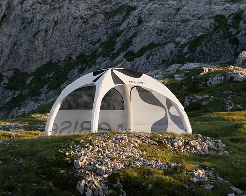 Weißes aufblasbares Zelt auf grüner Weise in felsiger Landschaft, bedruckt mit schwarzen Elementen