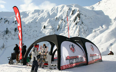Zwei schwarze aufblasbare Eventzelte mit bedruckten weißen Seitenwände, aufgebaut auf beschneiter Skipiste