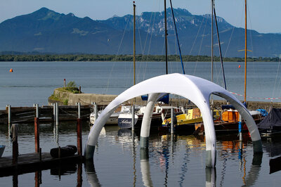 Weißes Luftzelt auf Wasseroberfläche des Chiemsees, Nahaufnahme.  Im Hintergrund Segelschiffe und Berge.