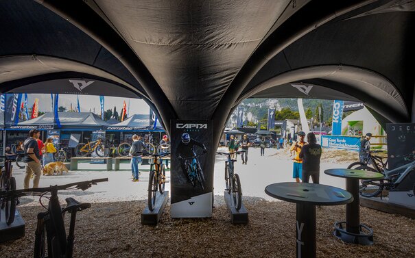 Aufblasbares Werbezelt in der Farbe Schwarz mit Bedruckung, darunter Fahrräder und Tische, davor weitere Zelte und Messebesucher*innen