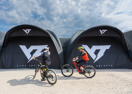 Zwei aufblasbare Werbezelte in der Farbe Schwarz mit weißer Bedruckung, davor zwei Fahrradfahrer