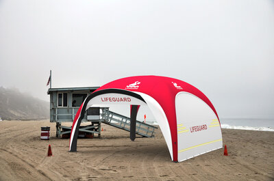 Red and white inflatable rescue tent with sidewalls on beach in cloudy weather