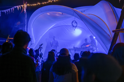 Violett beleuchtetes weißes Eventzelt als Bühne für eine Band, tanzendes Publikum, Nachtaufnahme 