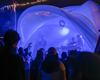 Violett beleuchtetes weißes Eventzelt als Bühne für eine Band, tanzendes Publikum, Nachtaufnahme