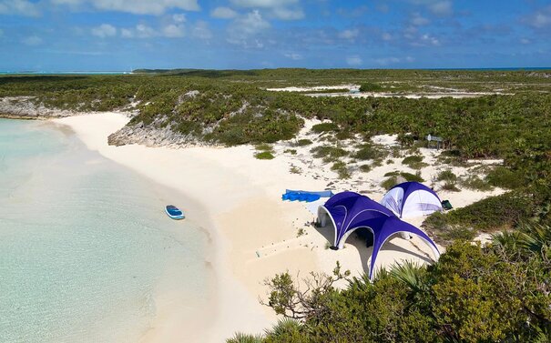 Personaliserte aufblasbare Zelte in den Farben Weiß und Violett an Strand, weißer Sand und glasklares Wasser, Vogelperspektive