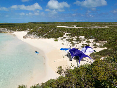 White and violet personalised inflatable tents on beach, white sand, clear water, aerial view